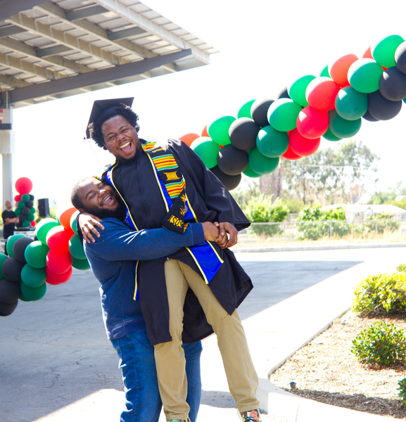 Black scholar being cheered by family, picked up in the air