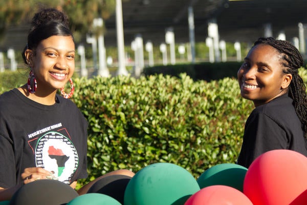 Two students with green and red balloons pose for a photo